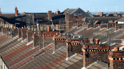 Image shows the roofs of terraced houses, with chimney pots and TV aerials disappearing into the distance. 