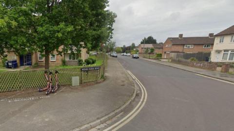 A view of Wood Farm Road on a cloudy day. There are three e-scooters parked near the street name sign