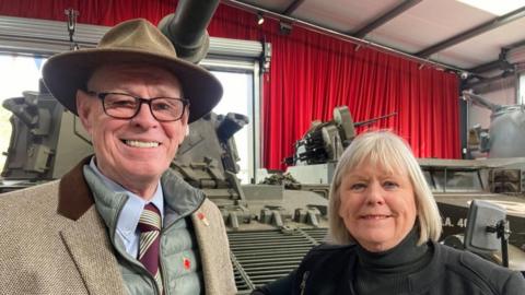 Siblings Howard Johnson and Paula Peace stand in front of a military-style green tank.