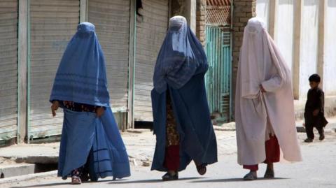 Afghan women wearing burqas travel in the back of a a mini truck 