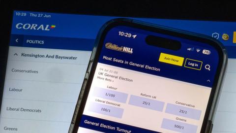 A phone and a computer screen with betting apps showing odds for political bets ahead of the forthcoming UK general election