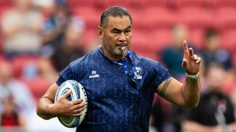 Pat Lam holds a ball in one hand and his finger up with the other and blows a whistle during a pre-game warm-up