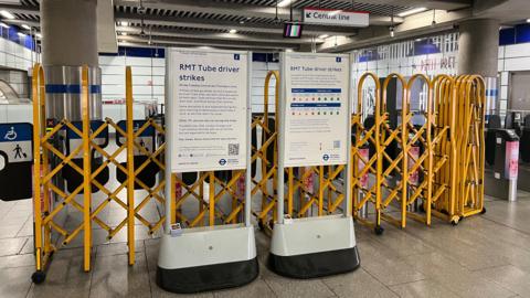 Signs about the Tube strike stand in front of closed barriers at the entrance to the Central line in Tottenham Court Road station