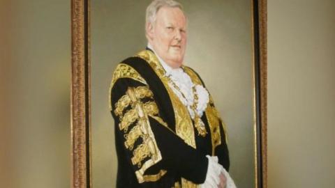 The portrait of Lord Wallace Browne. He is wearing a robe with golden ribbons and a gold medallion. 