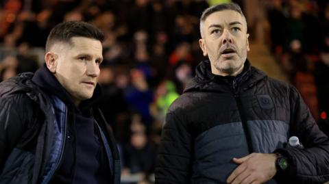 Ryan Dicker on the right of the picture talks to Crewe manager Lee Bell on the touchline during a match