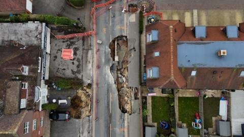 An aerial view of Godstone High Street showing the sinkholes. The street is cordoned off and houses line either side of the street.