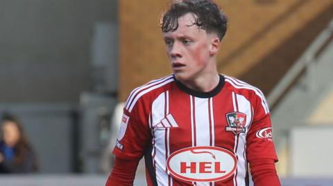 Ethan Brierley in action for Exeter City wearing their red and white striped home jersey