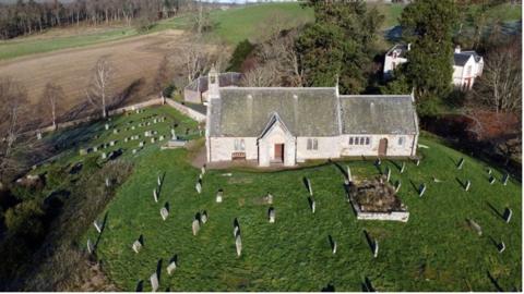 Church pictured from above in the sunshine on a hill surrounded by a graveyard.