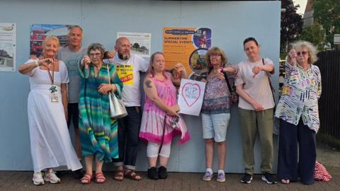 Campaigners stand outside the boarded up bus shelter in Sheringham pointing their thumbs down following the meeting