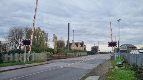 A railway crossing with red and white barriers lifted on either side.