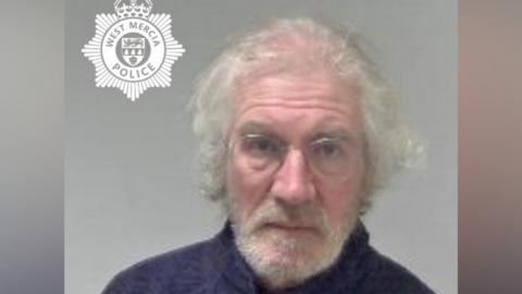 A custody image of Timothy 'Paul' Barnes. He wears thin-rimmed glasses and a zip up jacket