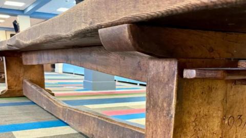 Wooden six metre-long 1937 'Mouseman' school dining table standing on a carpet in a large room.