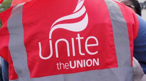 The back of a Unite the Union member who is wearing a red bib with the union's name written on it.
