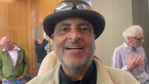 A man in a bowler hat looks into camera 