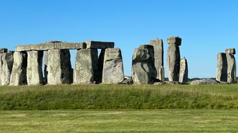 Stonehenge under a blue sky with grass in front.