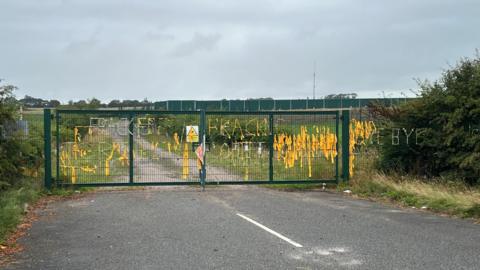 Many yellow pieces of paper tied to the green gate at the former fracking site