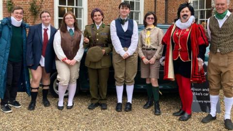 Eight members of the public dressed as characters from the 91ȱ sitcom Ghosts, standing outside the entrance to West Horsley Place, the filming location for the programme.