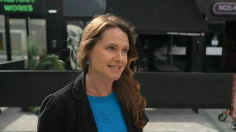 Sarah Chaundler outside the cinema wearing a blue top and black jacket. She has long wavy brown hair. 
