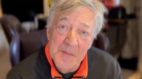 Stephen Fry - a man looking up into his web camera with the background blurred, but it looks like a study.