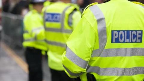 The backs of three police officers in yellow hi-vis jackets.