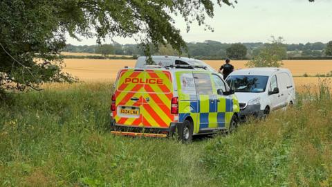 Three police vans parked on a field, with an officer looking away into the field.