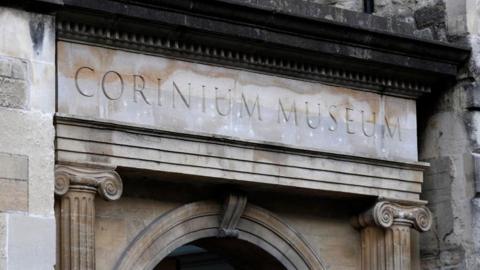 An exterior view of the Corinum Museum, showing a stone arch and the museum name carved in stone above