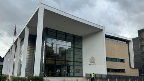 The front entrance to Ipswich Crown Court - a large building with a glass frontage, bordered by a white structure. 