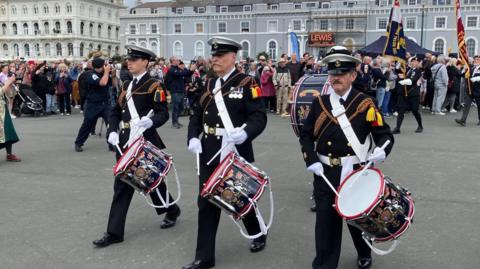 Three men dressed in military regalia holding drums on Plymouth Hoe.