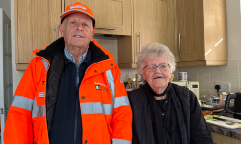 A man in s florescent coat and and an older lady dressed in black 