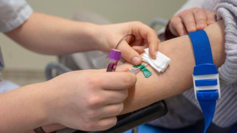 A healthcare professional draws blood from a patient's arm for a medical test in a clinical setting.