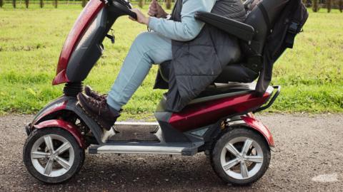 A stock photo of a woman on a powered mobility scooter outside in a park