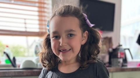 Bebe King, a young girl, has her hair tied up in bunches and is smiling at the camera.