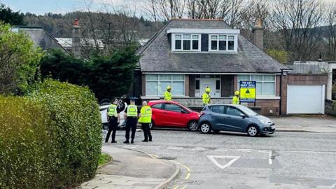 Emergency services at the scene of a crash, one white car is on its roof.
