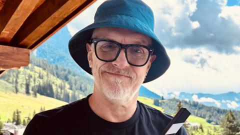 Greg Davies, wearing sunglasses and a blue bucket hat