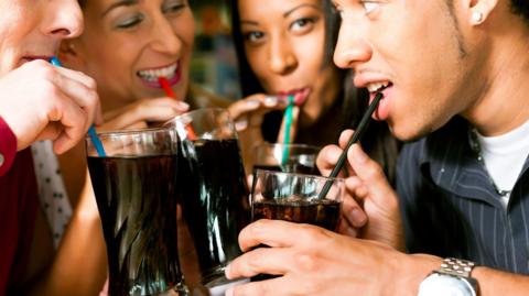 Four friends drinking soda in a bar with colorful straws