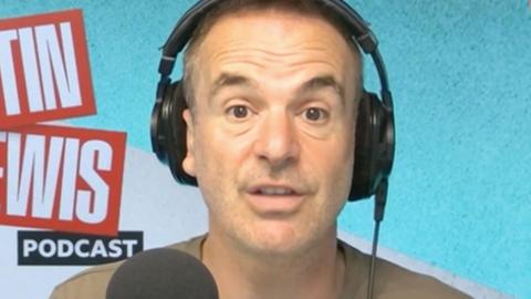 Radio host and money saving expert Martin Lewis wears headphones and talks into a microphone during his podcast.