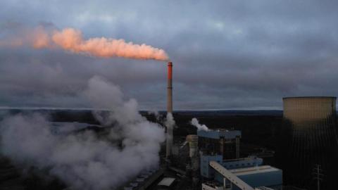 View of a coal-fired power station, with gases escaping from the top of a tall chimney as a white cloud