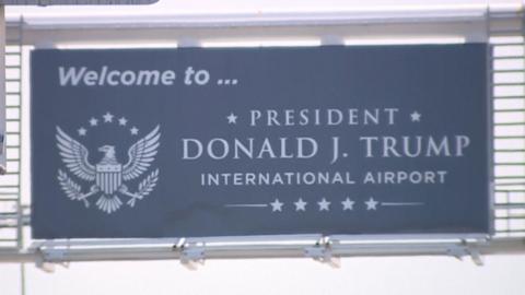 Image shows a sign saying "Welcome to President Donald J Trump International Airport"