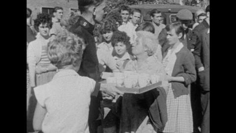 A man carries a tea tray, surrounded by people waiting for news 