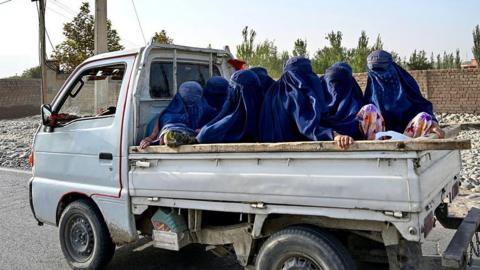 Afghan women wearing burqas travel in the back of a a mini truck 