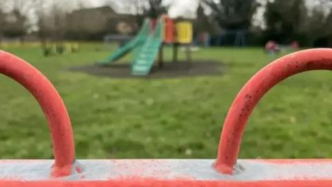 A playground with red metal fencing and a green slide in the background