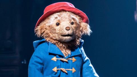 Paddington on stage in the West End, wearing his trademark blue coat and red hat