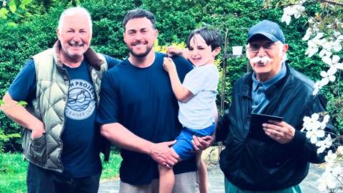 Arran Campolucci-Bordi is pictured holding his son and standing next to his father and grandfather in a garden. 