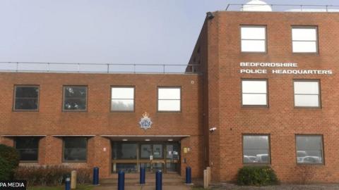 An external picture of Bedfordshire Police Headquarters - a red brick building with windows and glass doors.