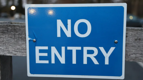 A blue square no entry sign has been pinned to a wooden fence.