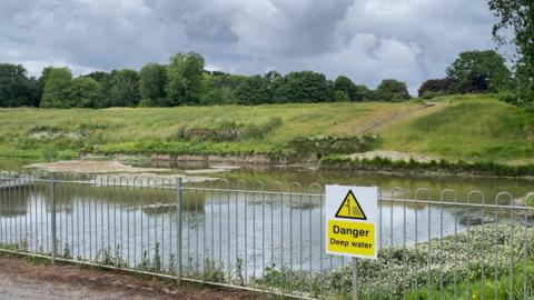 A pond with a grass bank and a sign saying Danger.