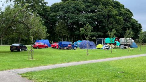 Tents pitched and vehicles parked on a grassed area of parkland