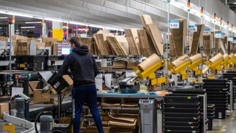 A worker at a warehouse packages items as they pass him on a conveyor belt.
