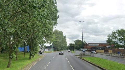 Stock image of Belle Vue Way, in Hartlepool, near the junction with Thomlinson Road. There are two lanes for traffic in either direction. A lorry is at the junction waiting to pull out.