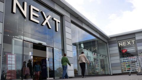 A Next store is seen with the logo looming large over passers-by as they walk outside the storefront on a sunny-cloudy day in Basildon in October.